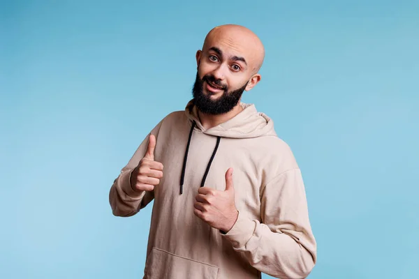 年轻面带微笑的Arab男人 用大拇指竖起的手势和积极向上的情绪表示接受 穿着休闲装的快乐的人 穿着类似标志的休闲装 看着相机 表示认可 — 图库照片