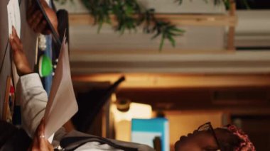 Atölyede tartışan dikey video ekibi yeni kıyafetler yaratmak için model ve taslak seçiyor. Tasarımcı ve asistan atölyede el işi aletleri kullanarak giyim markası üretiyorlar. El bilgisayarı