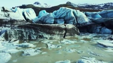 Güzel vatnajokull buzulu dron görüntüsü, devasa buz blokları ve mavi renkli buzdağları. Karlı dağları ve muhteşem donmuş kayaları olan muhteşem bir buzul gölü. 60 fps video.