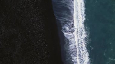 İzlanda siyah kumlu plaj hava manzarası, kıyı şeridine dalgaların çarptığı muhteşem Atlantik kıyıları. Kutup manzarası, karlı dağlar ve kumsaldaki siyah kumlar, soğuk manzaralar. 60 fps video.