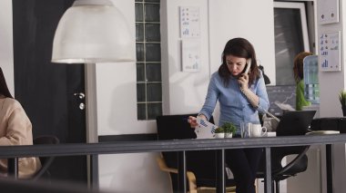 Executive manager talking on landline phone call and working on business investment. Employee using office telephone with cord to have remote conversation, chatting about report. Handheld shot.