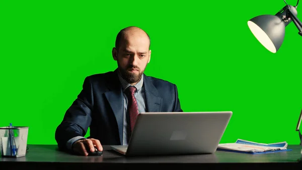 Entrepreneur looking at data on isolated greenscreen, and working on laptop. Young businessman in suit and tie standing over blank mockup and chroma key background, white collar.