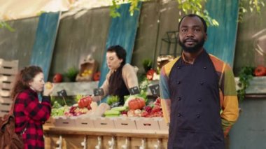 African american vendor selling fresh locally grown produce, presenting organic colorful fruits and vegetables. Young man greengrocer having local farmers market, small business. Handheld shot.