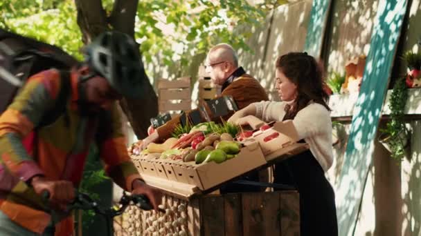 女摊贩给送水果和蔬菜的人下订单 拿食物给顾客 男性信使骑自行车 背着背包 健康的农产品递送 — 图库视频影像