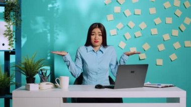 Şaşırmış iş kadını omuz silkiyor sorgulama hareketi yapıyor, karar veremiyor. Şaşırmış Asyalı ofis çalışanı modern parlak iş yerinde bir şeyden emin olamıyor.
