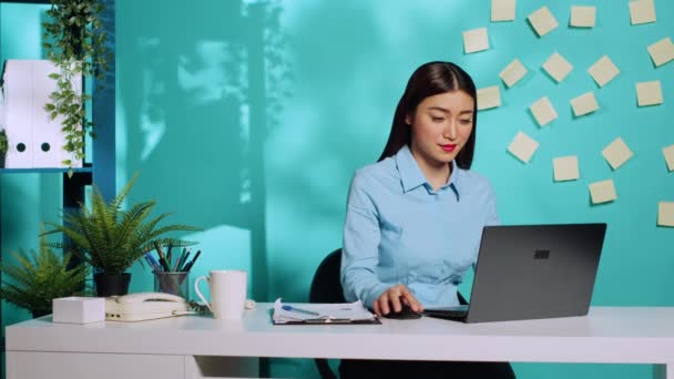 在交叉核对剪贴板数据笔记后 在笔记本电脑键盘上打字的女商人笑了 在蓝色工作室背景的现代创意写字台工作的有重点的专业员工 — 图库视频影像