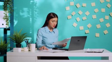 Odaklanmış iş kadını yönetici, evrak işleri ve dizüstü bilgisayar arasındaki idari verileri karşılaştırıyor. Modern işyerlerinde çalışan profesyonel ofis çalışanı.
