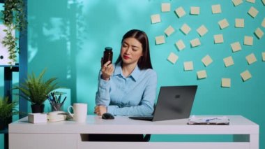 Kafası karışmış sekreter ilaç şişesi bilgilerini kontrol ediyor, hangi veriyi bilgisayara gireceği konusunda kafası karışık. Parlak renkli modern ofis masasında çalışan iş kadını.