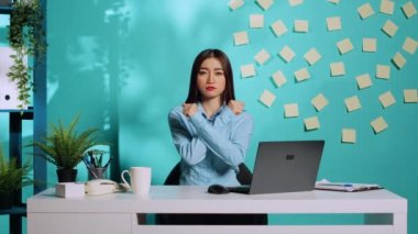 Asyalı iddialı çalışan hayır demekte kararlı, duruşundan emin, X işaretinde iki kolu çapraz tutuyor. Gergin ama kararlı ofis memuru stresli çalışma koşullarını reddediyor.