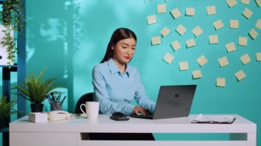 Gülümseyen iş kadını laptopta çalışırken telefonla kafa karıştırıcı bilgiler alıyor. Modern parlak ofis masasında çalışan profesyonel yönetici.