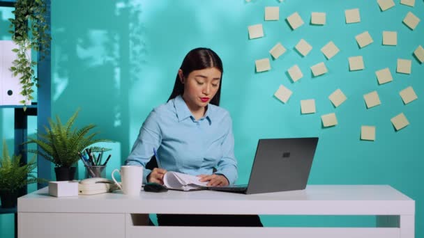 オンラインビデオ会議中にマネージャーから受け取った情報に続いて アジアの秘書はクリップボードの書類を完了します ブルースタジオを背景に現代オフィスの従業員女性 — ストック動画