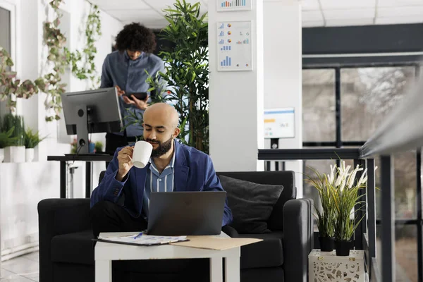 阿拉伯企业家一边享用咖啡 一边在笔记本电脑上做项目演示 坐在办公室沙发上 执行经理分析财务报告和喝茶 — 图库照片
