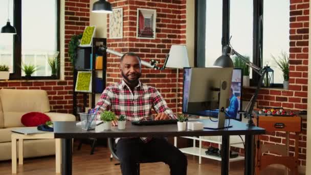 快乐的微笑着的非洲裔美国人 在家里工作 坐在写字台前 舒适时髦的公寓里 充满创意的折衷方案和室内设计 快乐乐观的远程工作的远程工作者 密切合作 — 图库视频影像