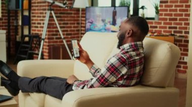 Neşeli yönetici, uzaktan çalışan meslektaşlarıyla akıllı telefondan video konferansı düzenliyor. Güzel, sade bir odada kanepede uzanmış, online video görüşmesi sırasında iş arkadaşlarıyla konuşuyor.