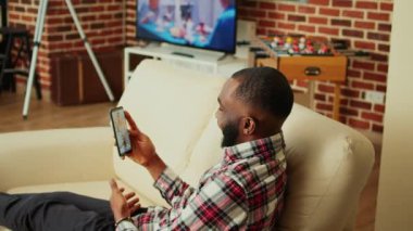 Şık, sade bir odada kanepede uzanmış, video konferans sırasında iş arkadaşlarıyla tartışıyor. Gülümseyen yönetici akıllı telefondan uzaktan çalışan meslektaşlarıyla çevrimiçi video görüşmesi yapıyor.