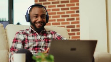 Oyuncu çevrimiçi video oyunu yarışması izliyor, favori beyaz takımın oturma odasında oturmasını destekliyor. Kulaklık takan bir adam, online içeriği izlemek için heyecanlı, el kamerasıyla çekilmiş.
