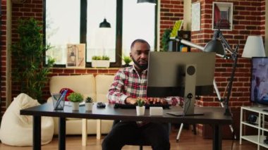 Sıcak, rahat bir dairede uzaktan çalışan bir çalışan. Neşeli gülümseyen serbest çalışan e-postaları cevaplayan, klavyeye yazan, modern oturma odasında telgraf çeken