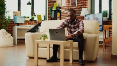 Kanepede uzanan tele-operatör, kişisel ofiste uzaktan görevleri yerine getiriyor. Rahatlamış serbest çalışan bilgisayarına veri yükleyen ve evde çalışırken bir fincan kahvenin keyfini çıkaran, el kamerasıyla yakın çekim yapan