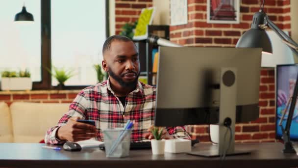 アフリカ系アメリカ人の男性は 現代的なスタイリッシュなアパートのリビングルームにいる間にウェブサイト上で支払い方法を追加します 陽気な男がオンラインショッピングを行うには 慎重にクレジットカード情報を入力興奮 — ストック動画