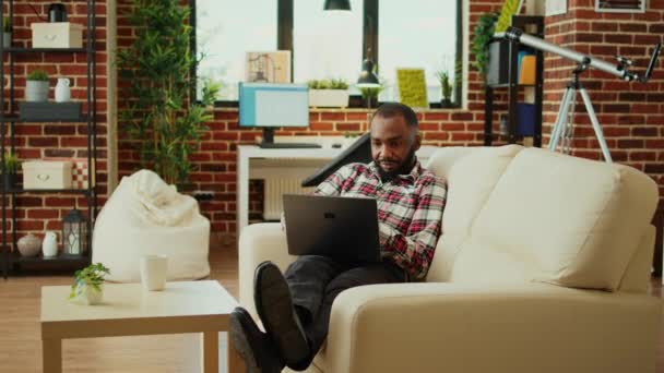 Uvolněný Africký Pracovník Který Při Ležení Gauči Kontroluje Emaily Notebooku — Stock video
