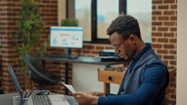 Başlangıç yöneticisi dizüstü bilgisayar ve belgelerle proje planı üzerinde çalışıyor, iş geliştirme evraklarını inceliyor. Analiz ve veri sonuçlarını kontrol eden genç bir yetişkin. El kamerasıyla..