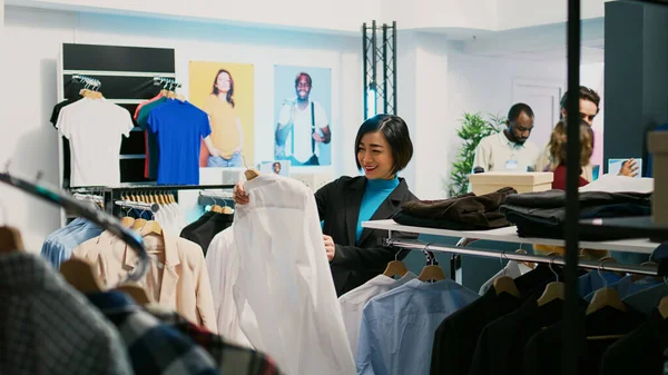 アジアのお客様は ハンガーに正式な服を検討し 小売店から新しいコレクションを購入します 流行の近代的な商品 商業活動をしようとする若い大人の訪問服店 — ストック写真