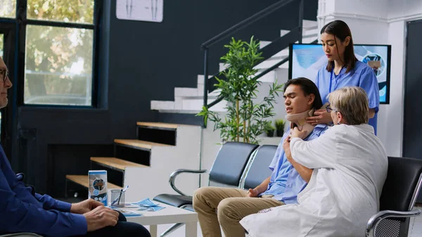 首の骨折後の回復を試みながら 患者が子宮頸部の襟を取るのを助ける看護師と医療 病院の待合室で健康診断を受けるアジア人男性 医学の概念 — ストック写真
