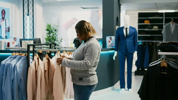 陽気な女性は ショッピングセンターでハンガーに流行の商品を見て 服にしようとする部屋に合うようになります 若い大人の服店でドレスアップ カジュアルウェアのためのショッピング — ストック写真