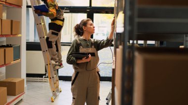 Tablet tarayıcıyla lojistik üzerinde çalışan kadın denetçi kutulardaki barkodları kontrol ediyor. Depo deposunda stok ürünleriyle paketleri inceleyen kadın çalışan..