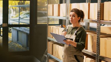 Depodaki lojistik stok listesini inceleyen kadın, tedarik zincirini kontrol ediyor. Depo müdürü envanter ve perakende satış ve nakliye malları için ürünleri denetliyor. El kamerasıyla..