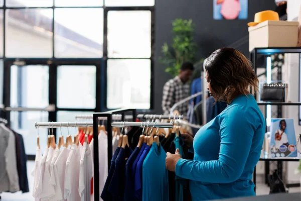 在现代精品店里 非洲裔美国人的顾客看到的衣架都是时髦的衣服 他们在购买时髦的商品 购物狂女人检查新的时装系列 分析面料 — 图库照片