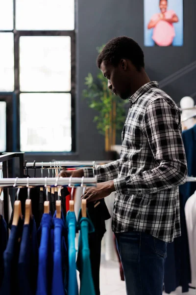 現代のブティックでカラフルな服を見て 流行のワードローブのためのアフリカ系アメリカ人の顧客ショッピング カジュアルウェアを購入するお店の男性は 衣料品店で新しいファッションコレクションをチェック — ストック写真
