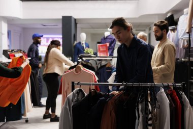 Çeşitli insanlar kıyafet dükkanından alışveriş yapıyor, ateşli Kara Cuma anlaşmaları arıyorlar. Moda mağazasında elbise askılarına bakan müşteriler, outlet mağazasında yeni moda koleksiyonlarını keşfediyorlar.