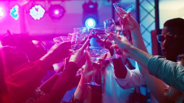 Group of friends clinking glasses at dance party, serving alcohol drinks and saying cheers in discotheque. Cheerful people dancing and having fun at club, entertainment. Handheld shot. clipart