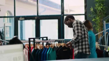Siyah gömlek için alışveriş yapan Afrikalı Amerikalı müşteriler modern butikte moda kıyafet malzemelerini analiz ediyorlar. Alışverişkolik adam günlük giysiler alıyor, yeni moda koleksiyonu olan askılara bakıyor.
