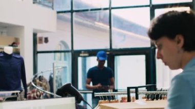 Afro-Amerikan kurye tablet bilgisayardan depo çalışanına teslimat raporunu gösteriyor, paket detaylarını modern butikte tartışıyor. Çalışan alışveriş merkezinde müşterileri çevrimiçi olarak hazırlıyor.