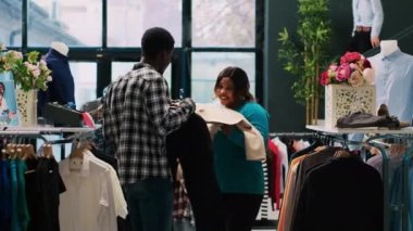 Neşeli çift şık mallarla oynuyor modern butikte modaya uygun kıyafetlerle oynuyorlar. Afrikalı Amerikalı müşteriler yeni gardırop için şık eşyalar alıyorlar. Moda konsepti