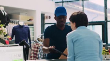 Modern butikte teslimat üniforması içinde kurye mağaza müdürüyle paket sevkiyatı detaylarını tartışıyor. Afro-Amerikan kurye tablet bilgisayarda dağıtım raporu gösteriyor. Moda konsepti