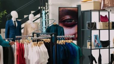 Afrikalı Amerikalı çift, mağaza müdüründen modern butikte kumaş parçalarını tartışarak şık ürünler için yardım istiyor. Neşeli müşteriler moda kıyafetler ve aksesuarlar için alışveriş yapıyor.