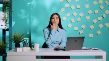 Neşeli, şakacı ofis çalışanı işteyken komik öpücükler yolluyor. Neşeli, neşeli iş kadını. Mavi stüdyo arka planında rahat, renkli iş yerinde eğleniyor.