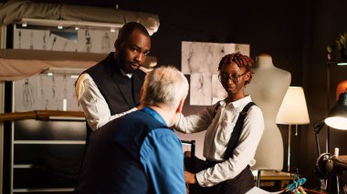 Erkek müşteri atölyede ceket deniyor. Uygun ve boyutta olduğundan emin olmak için. Deneyimli tasarımcı ve asistan atölyede kişisel ölçülere sahip özel yapım ceket tasarlıyor. Üçayak atışı.