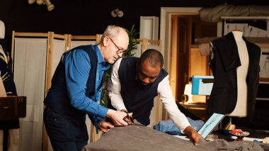 Terzi ve öğrenci atölyede kumaş kesiyor, yeni moda ürünleri yaratmak için kesim malzemesi kullanıyor. Deneyimli bir zanaatkar, yeni başlayanlara atölyede giysi el sanatları öğretiyor. El kamerasıyla..