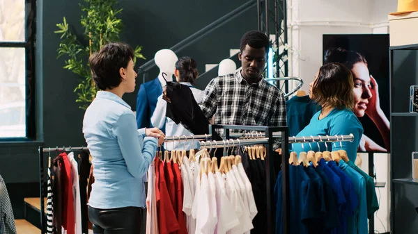 アフリカ系アメリカ人のカップルは モダンなブティックでアイテム生地を議論し スタイリッシュな商品の助けを店長に求めています 流行の服やアクセサリーのための陽気な顧客のショッピング — ストック写真