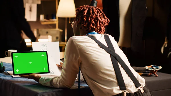 年轻的裁缝在工作室里检查绿色屏幕 在工作台上使用隔离的彩色键显示 专业设计人员使用平板电脑 手工操作的模型模板 — 图库照片