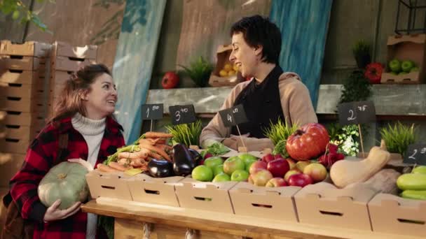 カウンターから新鮮な有機エコ製品を提供する女性ストールホルダーは 健康的な食事や地元の自然野菜についてクライアントに話しています バイオ製品について中小企業経営者に尋ねる陽気な女性 — ストック動画