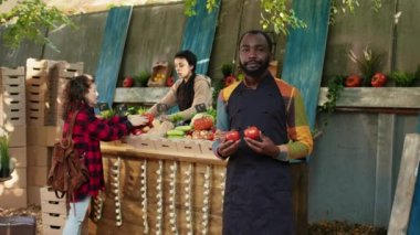 Afrika kökenli Amerikalı çiftçi, çiftçi pazarında taze eko ürünler sunuyor ve müşterilerle konuşuyor. Dışarıdaki pazar yerinde, yerel yetiştirilmiş organik meyve ve sebzeler, market sahibi....