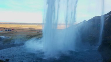 Seljalandsfoss büyük İskandinav çağlayanı Mart 2023 suları İzlanda 'da tepeden aşağı akıyor. Uçurumdan düşen nehir akıntısı ve İskandinav çağlayanı ile görkemli bir manzara. El kamerasıyla..