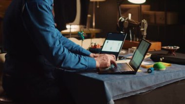 Eski terzi, dizüstü bilgisayar ve tabletteki modern takım elbise tasarımlarını karşılaştırarak kıyafet koleksiyonunda çalışıyor. Tecrübeli moda tasarımcısı yeni giyim markası için eskizlere bakıyor..