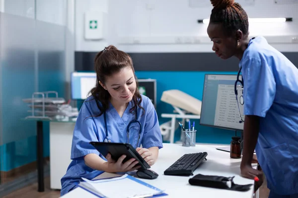 stock image Medical team of nurses working on tablet in modern professional medical office. Smiling healthcare employee comparing data with african american coworker in hospital workplace