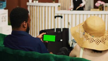 Telefondan yeşil ekranı kontrol eden turistler, egzotik sahil beldesine ulaşıp boş kromakey kopyalama alanına bakıyorlar. Otel müşterileri resepsiyonda izole edilmiş bir şablon kullanıyor. Üçayak atışı.